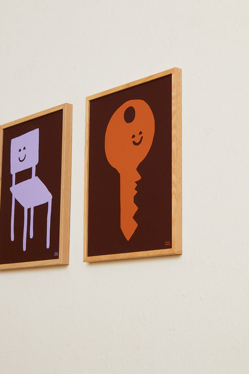 Two framed illustrations of a chair and a key on a beige wall.