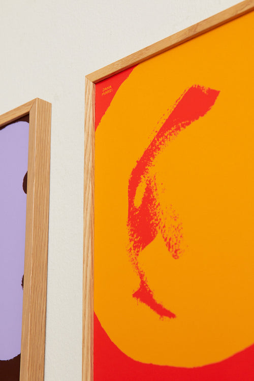 Two framed artworks, one with a purple abstract design and the other with a red and orange abstract design, on a light beige wall.