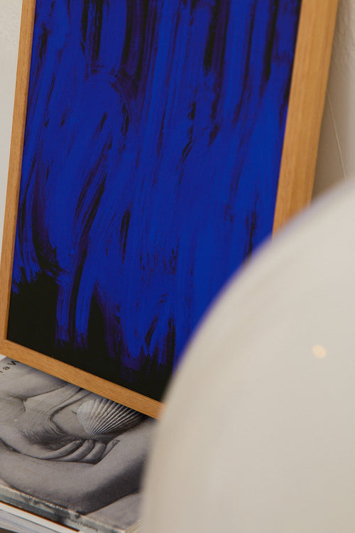 Framed abstract artwork with a blue and black design on a white wall.