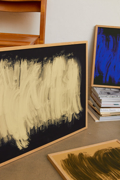 Three abstract paintings in wooden frames on a surface.