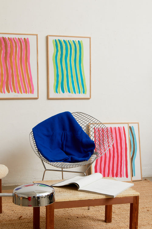 Two abstract striped art prints in oak frames on a light wall, styled above a wooden coffee table with a chair and woven rug.