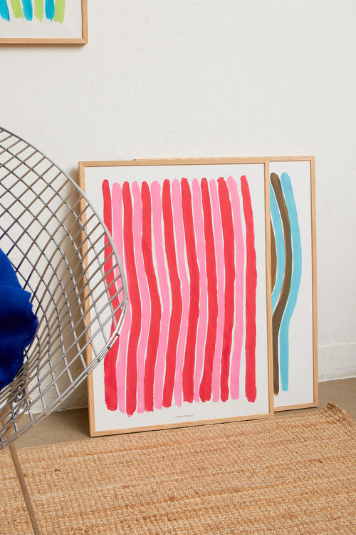 Two abstract striped art prints in oak frames leaning against a light wall.
