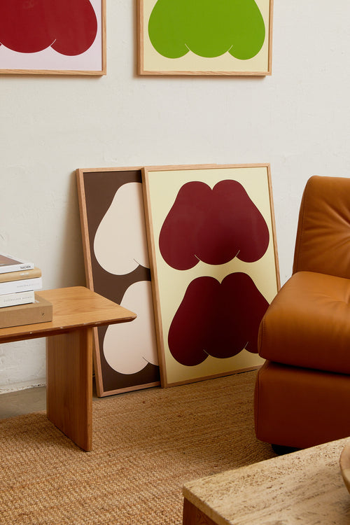 Art print featuring playful, bold typography of the text “MM”, the sound of enjoyment, in burgundy against a yellow-beige background. Styled in a minimalist interior.