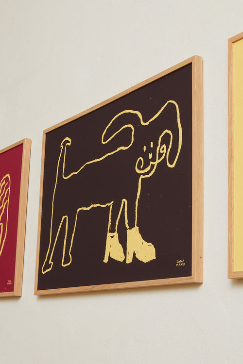 Angled side view of the framed dark brown dog print displayed on a light wall