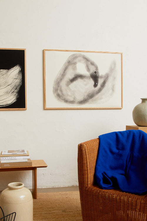 Art print with a stylized illustration of a swan in gray tones against a, with a soft and graphic expression. Styled in a minimalist interior.