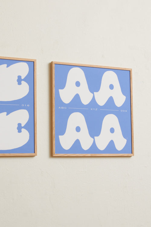 Square-format Art print with a graphic interpretation of the letter “A”. Created in white against a calm blue, lightly grain-textured background. Styled in a minimalist interior.