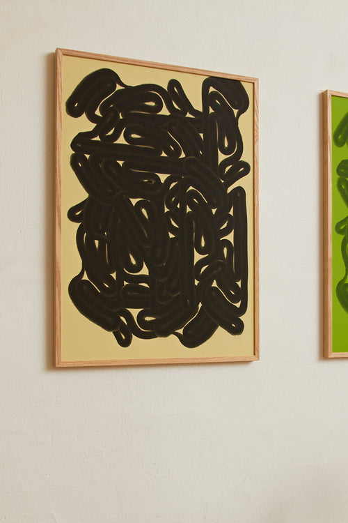 Art print featuring dense, black rounded forms with a smooth, glossy feeling emerging against a warm, light yellow background. Styled in a minimalist interior.