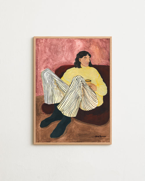 Framed artwork of a woman sitting on a couch with a warm color palette.