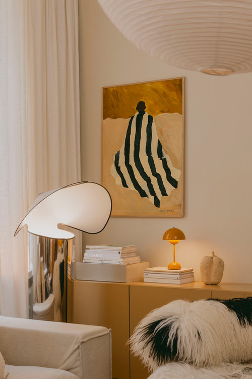 Modern living room with a lamp, books, and a painting on the wall.