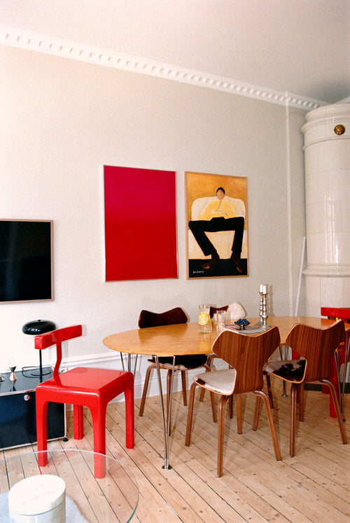 Dining area with a red chair, wooden table, and chairs against a white wall with abstract art.